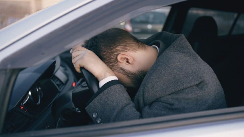 Man slumped forward onto his steering wheel, seemingly distressed or sleeping inside a car.