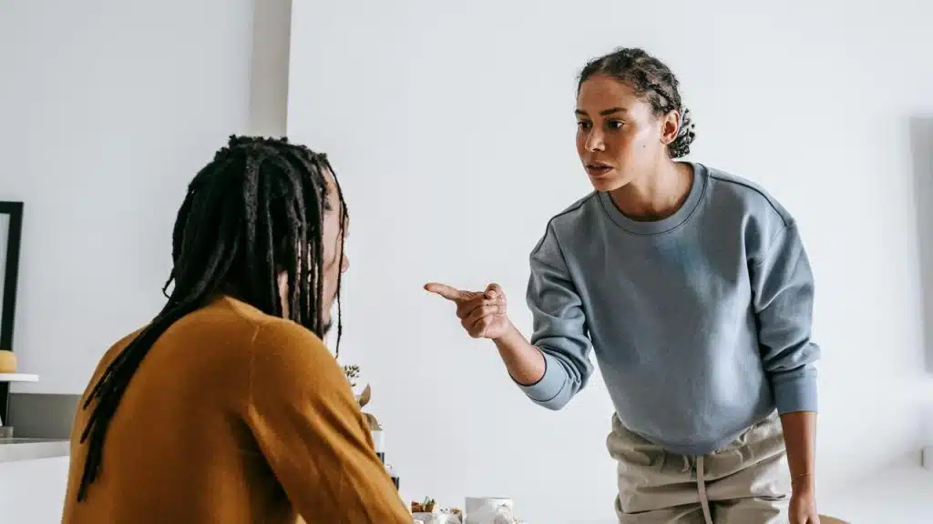 A woman standing and pointing her finger while arguing with a man sitting at a table.