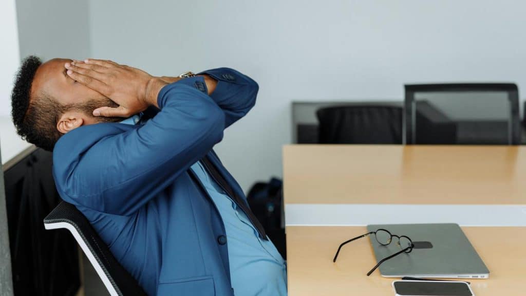 A man sitting at a desk covering his face with his hands.