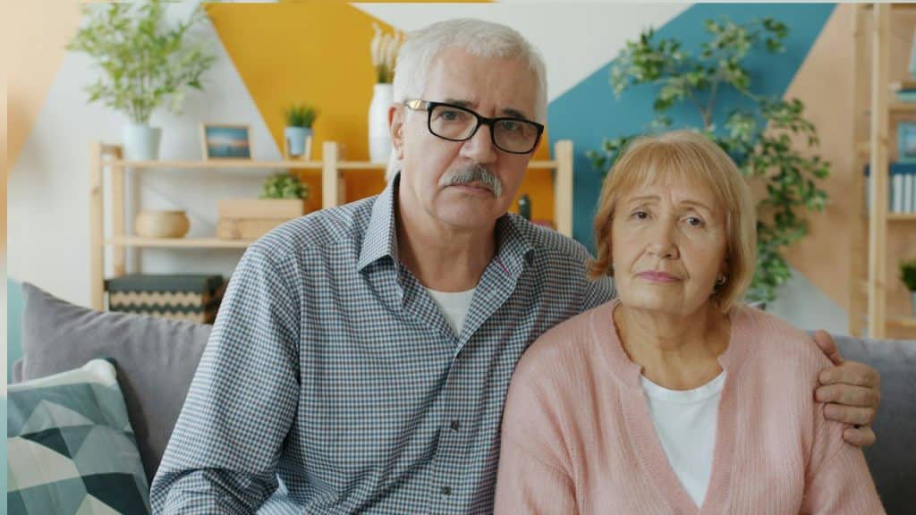 An Elderly couple sitting silently on a couch indoors.
