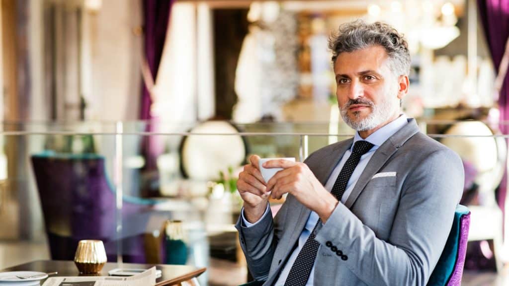 A Confident man in a grey suit sitting and holding a cup.