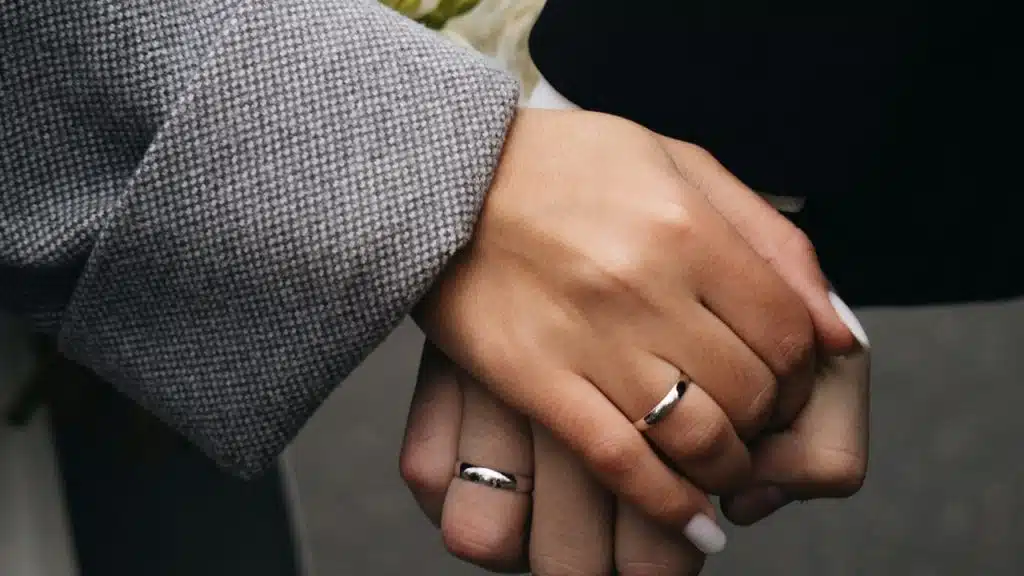 A couple wearing wedding rings and holding hands.