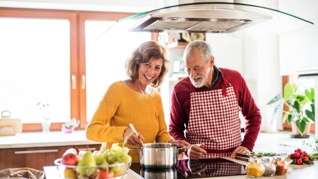 Smiling older couple cooking together in a bright, modern kitchen.