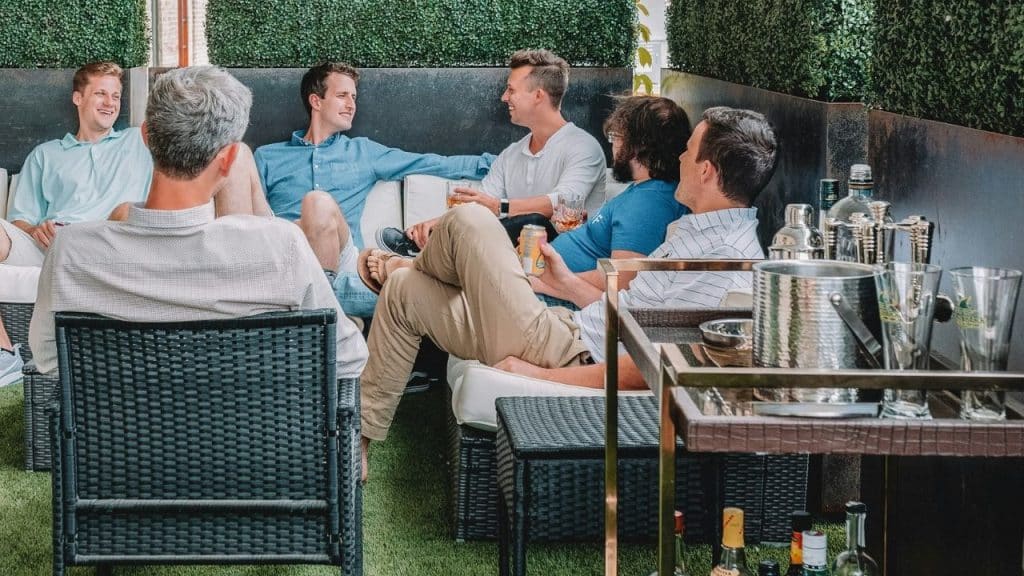 Group of six men socializing on outdoor patio furniture with a bar cart.
