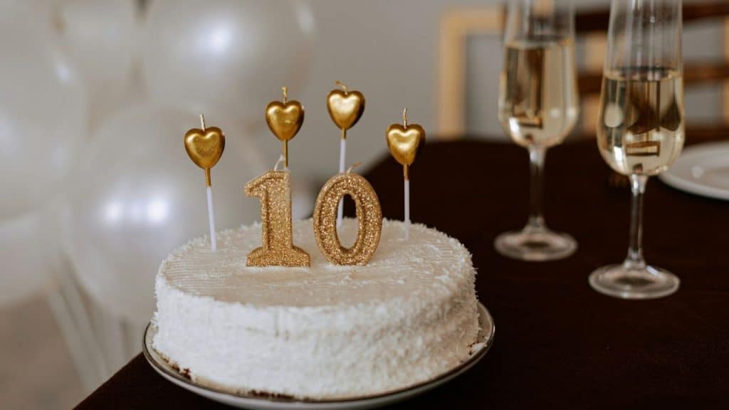White cake topped with a glittery number 10 and four gold heart candles.