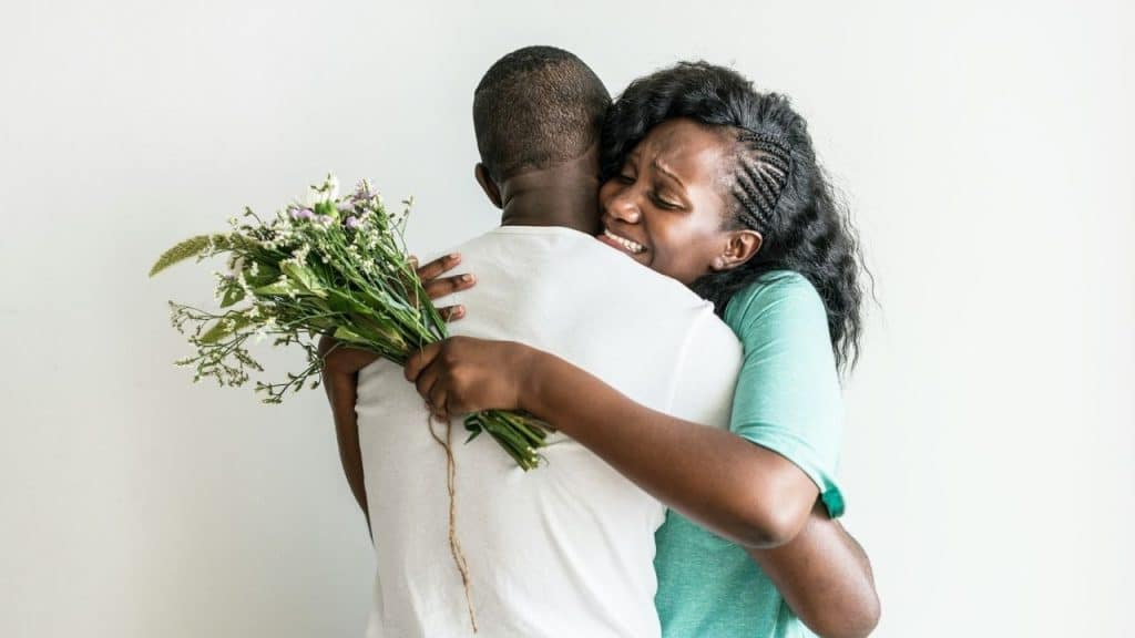 Woman tearfully embracing a man while holding a bouquet of wildflowers.