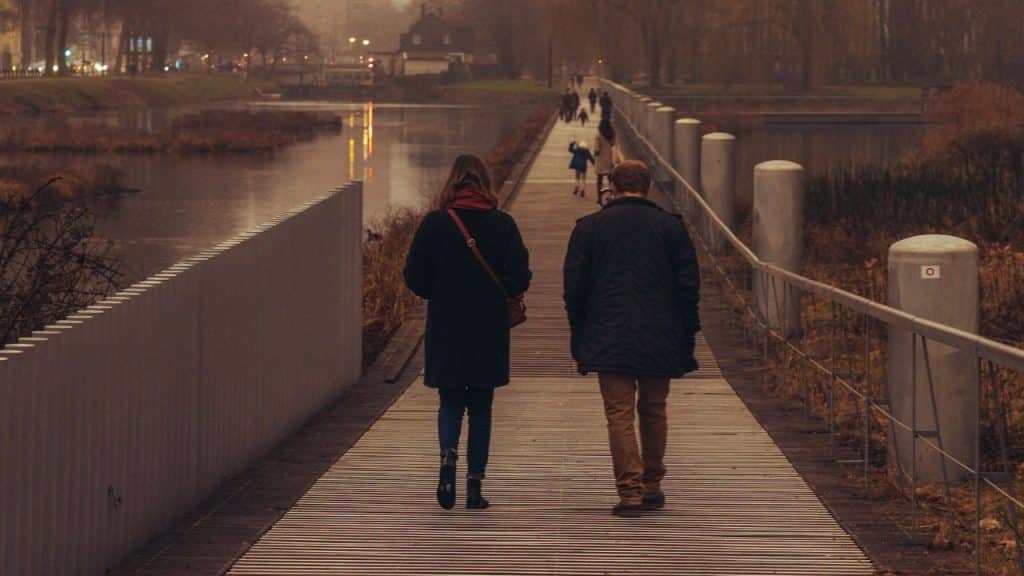 A couple walking away on a long, narrow boardwalk bridge over water on a cloudy day.