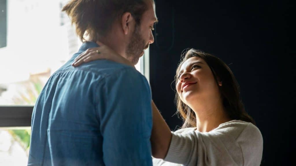 A woman smiling up at a man in a blue shirt with her arm around his neck.