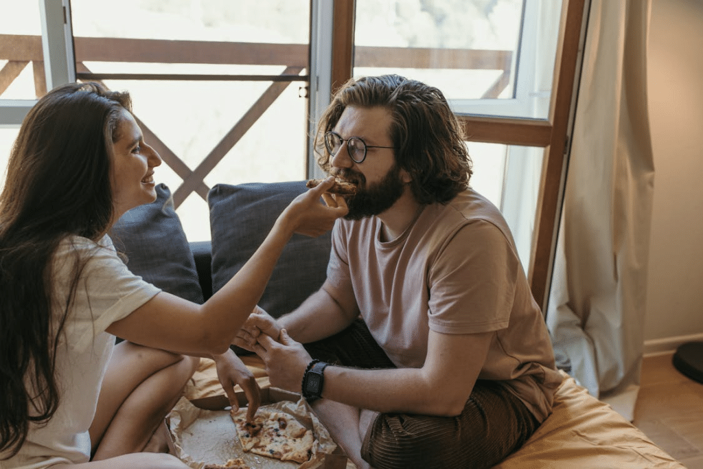 A Couple Easting Pizza Near a Window