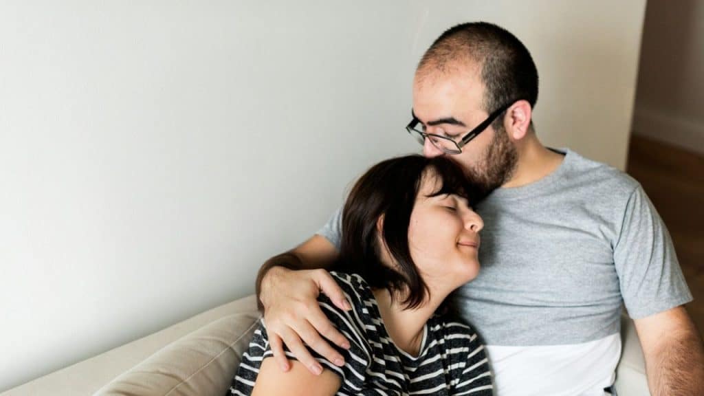 A man with glasses is embracing and kissing a woman's forehead.