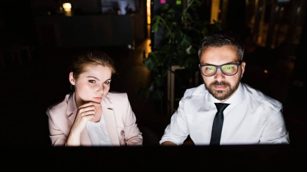 Two people, a woman and a man, working intently in a dark office environment.