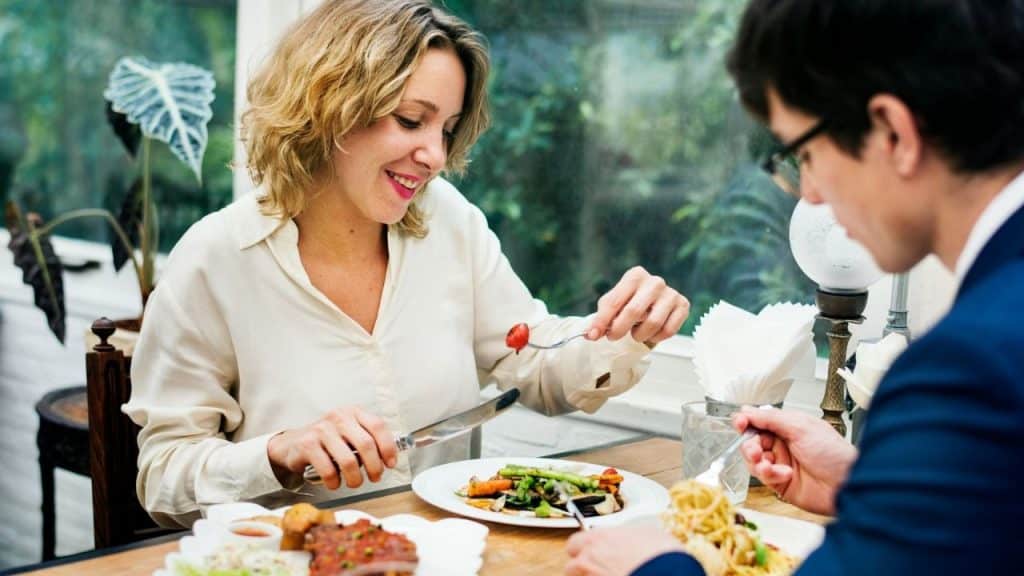 A smiling woman and a man eating a meal together at a restaurant.