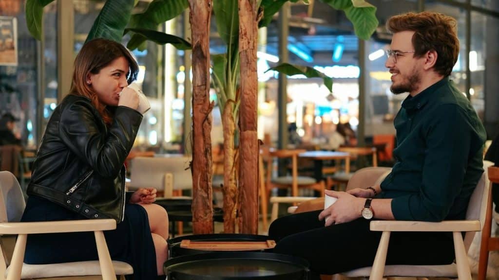 A man and woman smiling at each other while having coffee at a cafe.