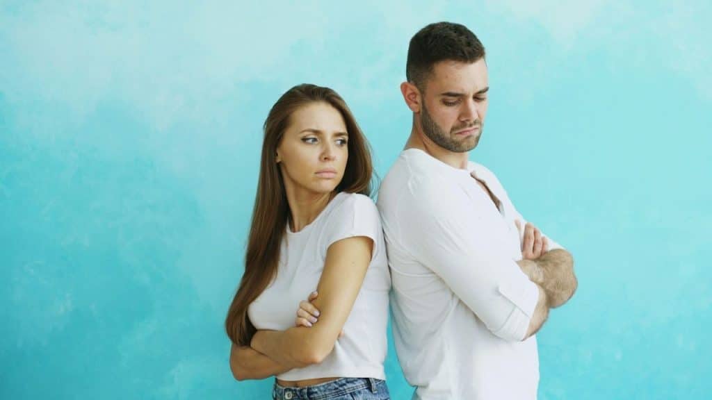 A man and a woman standing back-to-back with arms crossed, looking annoyed.