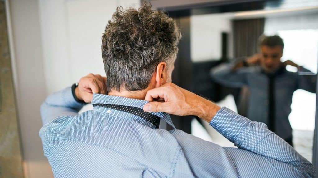 A man seen from behind adjusting his collar in front of a mirror.