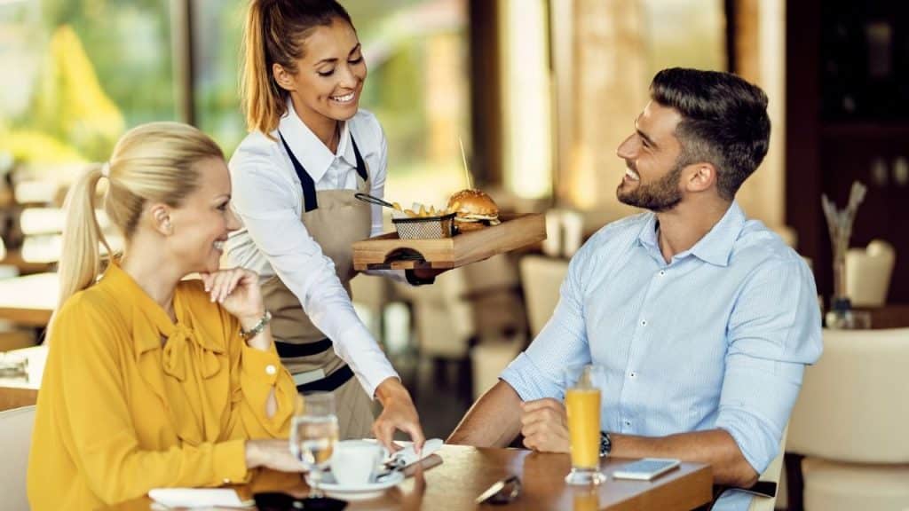 A waitress serving food to a smiling man and woman sitting at a table.