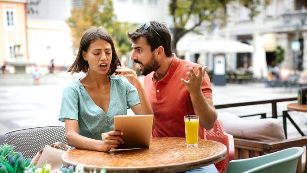 A frustrated man talking loudly to a woman holding a tablet at a cafe.