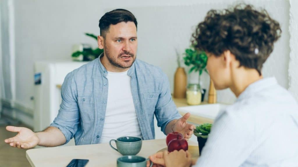 A man with an intense expression talking to a woman across a table.