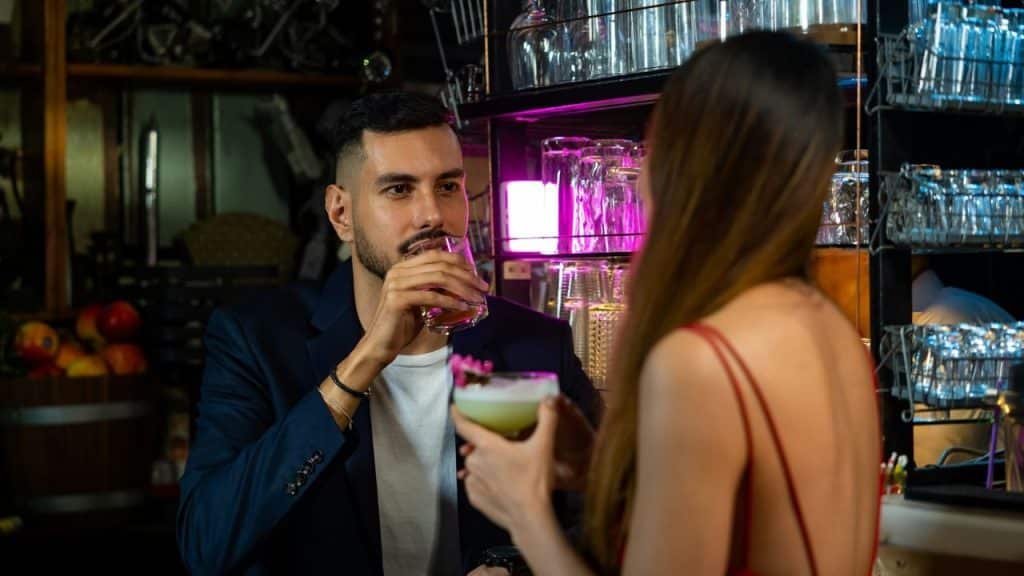 A man and woman having drinks at a bar, looking at each other.