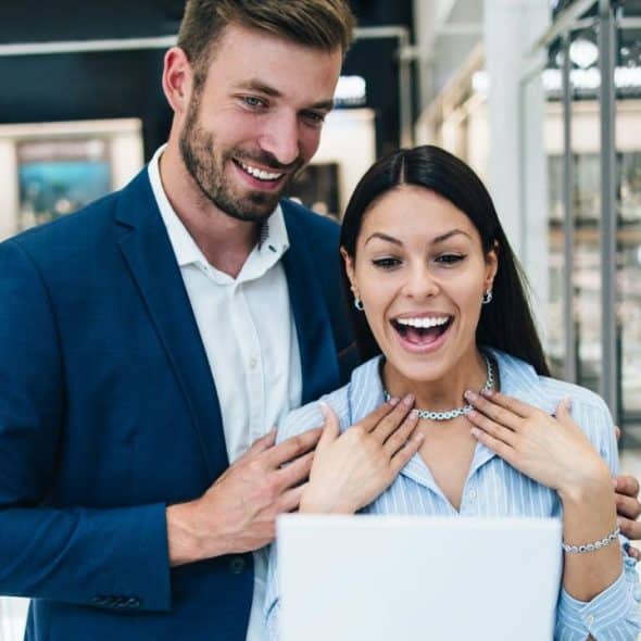 A surprised woman with a necklace and bracelet looking at a screen in a store.