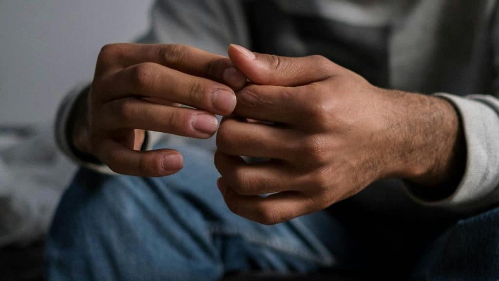 A man sitting with his hands clasped, appearing anxious or deep in thought.