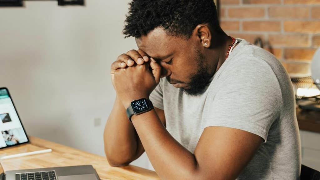 A man sitting at a desk with his head resting on clasped hands.