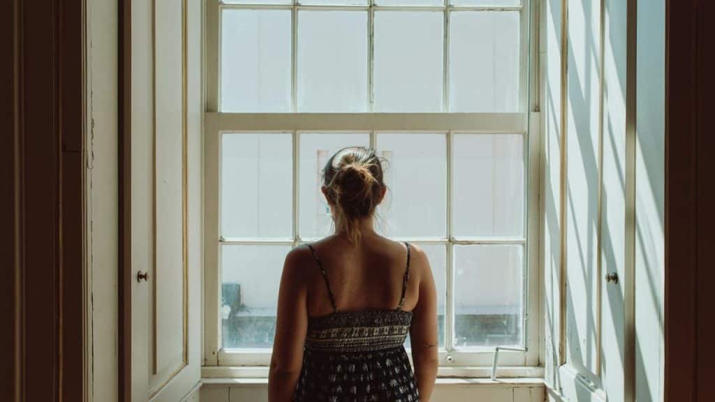 A woman standing by a window and looking outside.