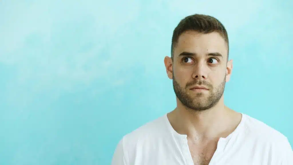 A man looking nervous and standing in front of a blue background.