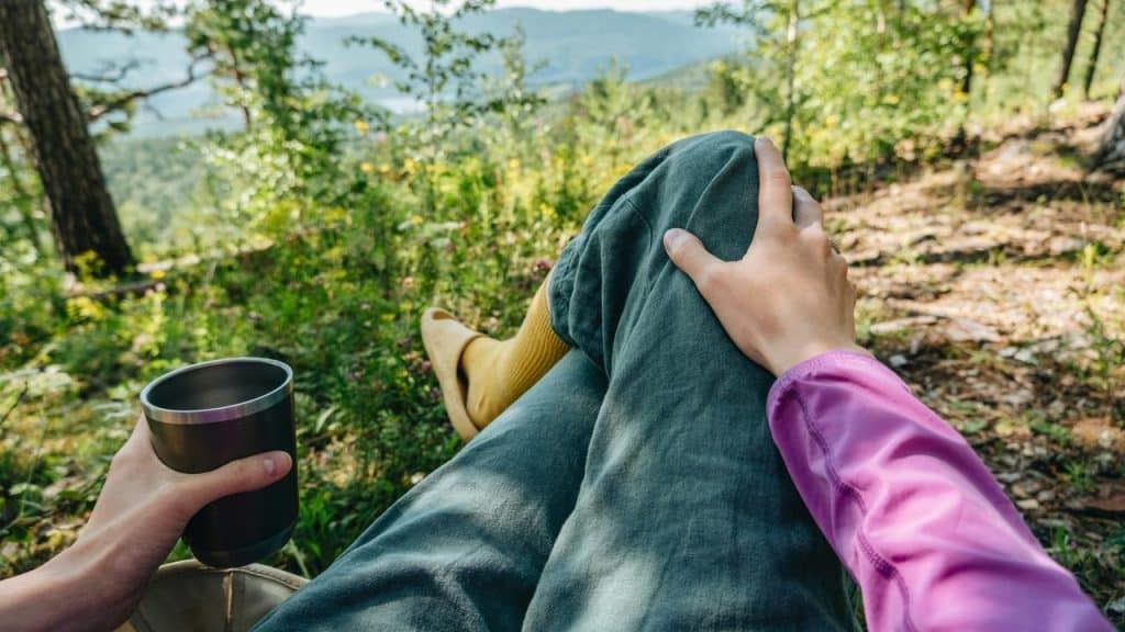 A person relaxing outdoors with a drink and a scenic mountain view.