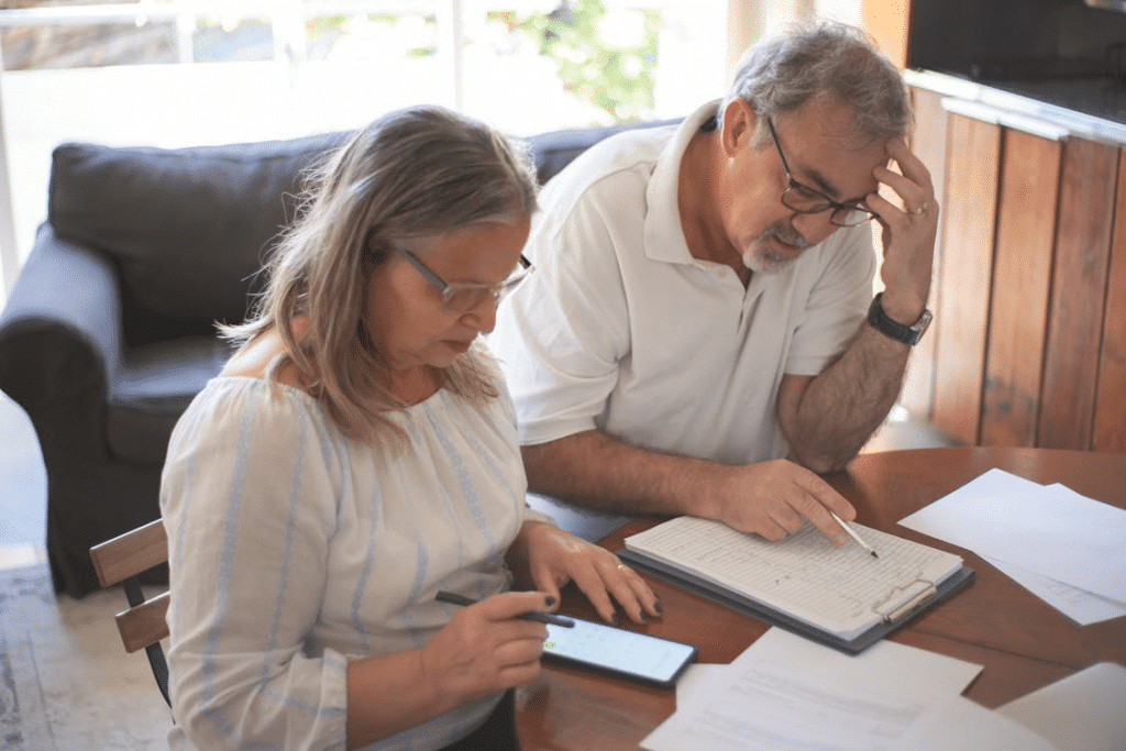 Elderly Couple Sitting at the Table with Documents and Using a Smartphone