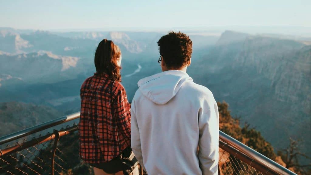 A couple stands at a scenic overlook admiring a vast mountain view.