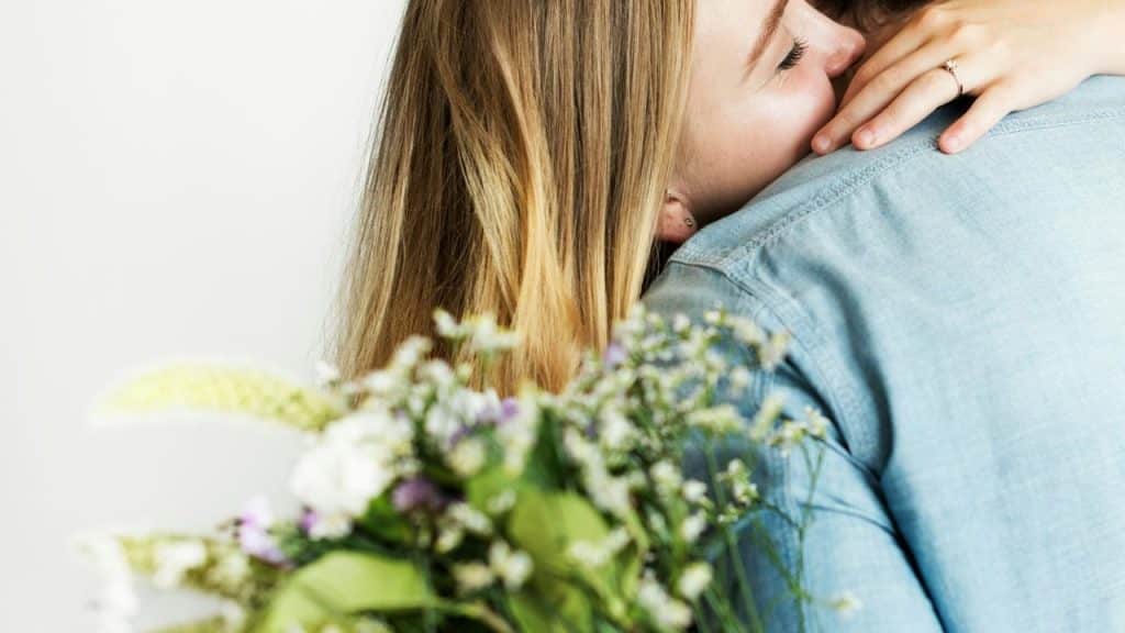A woman hugs someone while holding a bouquet of flowers.