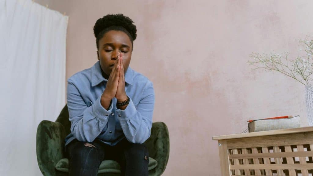 A person sits with their hands together, appearing to pray or reflect.