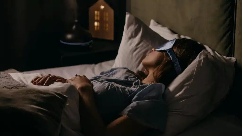 A woman wearing a sleep mask rests in bed at night.