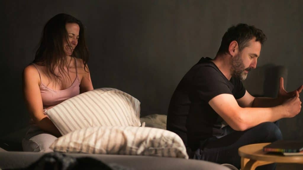 A woman is crying and appearing distressed while a man sits with his back to her.