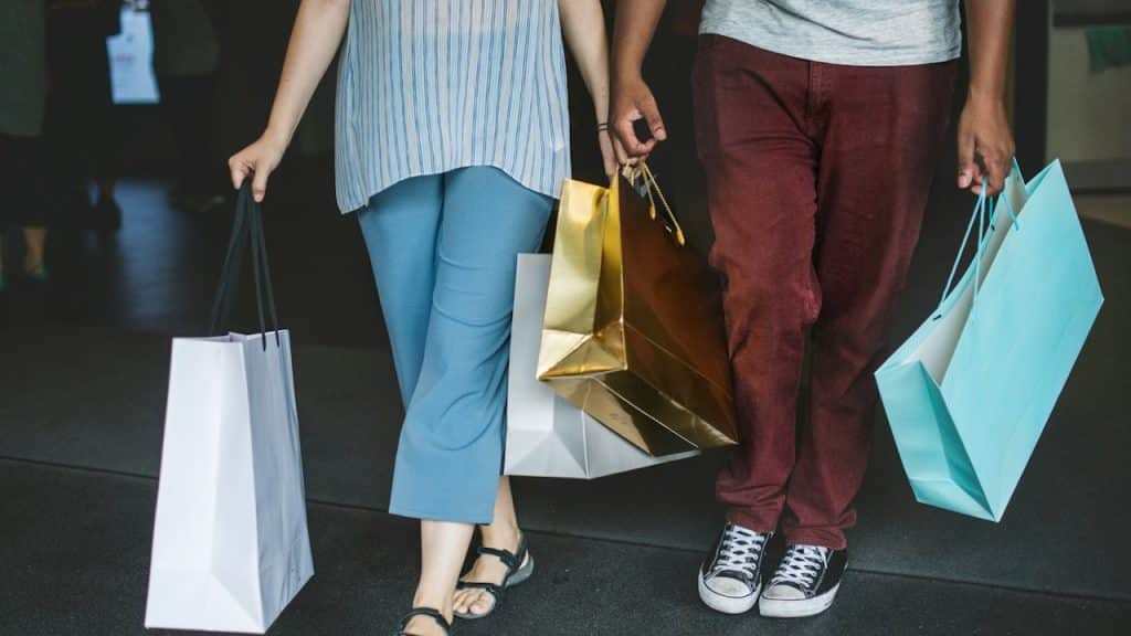 A low-angle shot of two people walking together, holding several shopping bags of various colors.