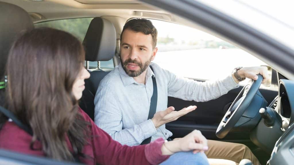 A man driving a car is gesturing and talking to a woman in the passenger seat.