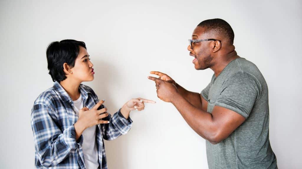 A woman and a man are facing each other and arguing, with both pointing their fingers and using expressive hand gestures.