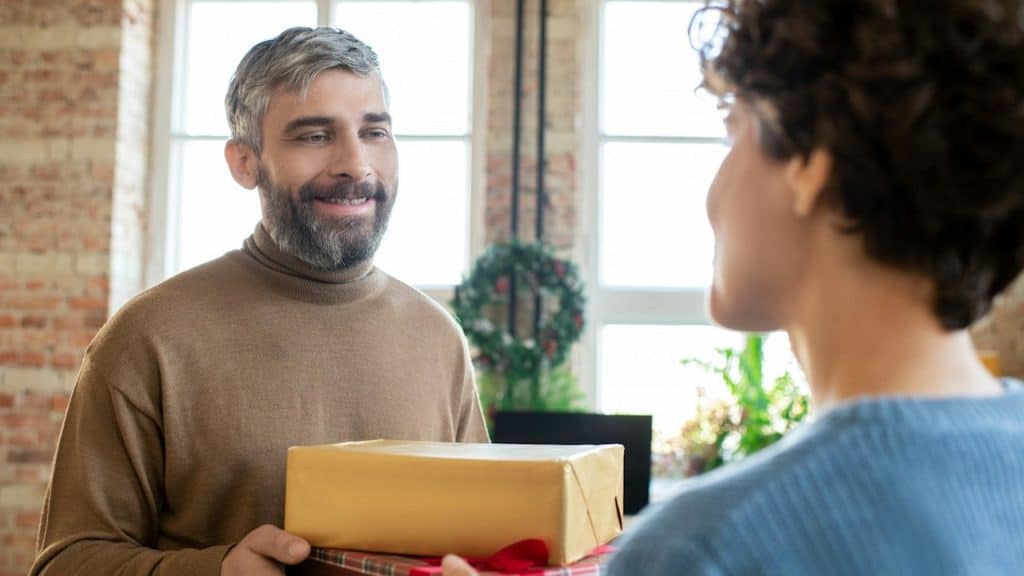 A man with a graying beard receiving gifts from a woman.