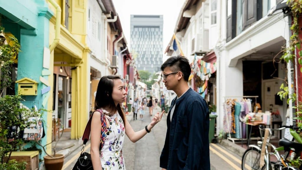 A woman talking to a man and gesturing with her finger while they stand in a street.