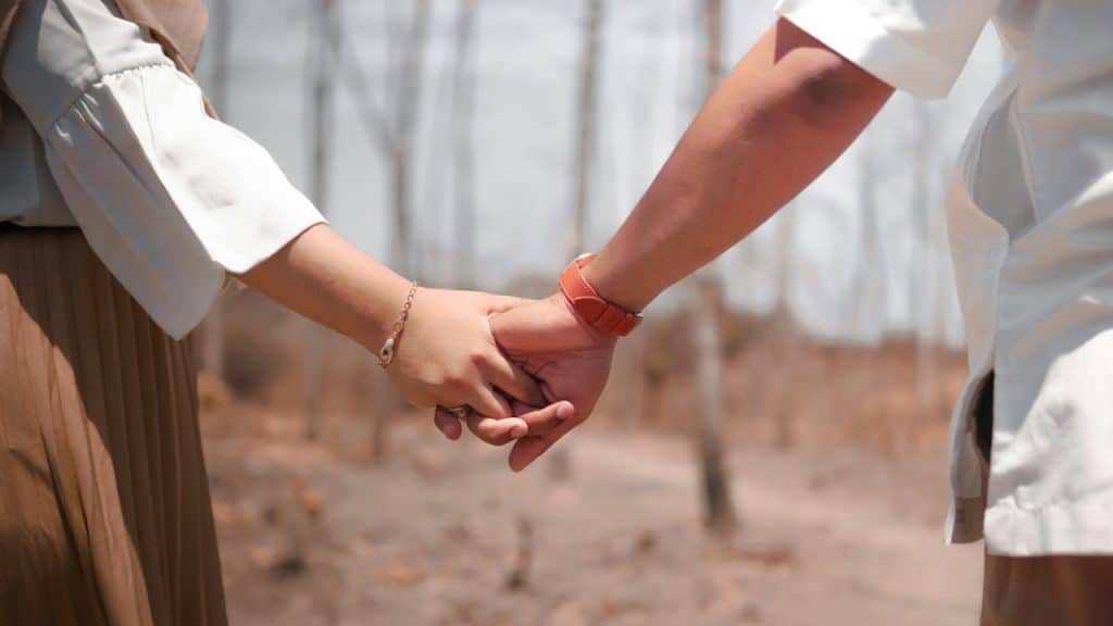 A couple holding hands, with the woman wearing a bracelet and the man wearing a watch.