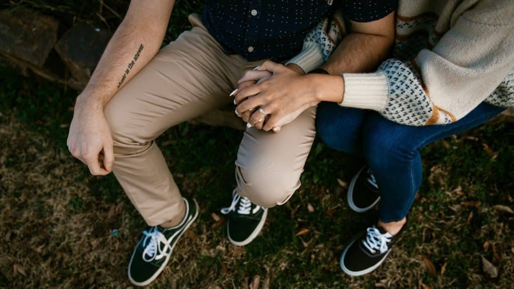 An overhead close-up of a couple sitting outdoors, holding hands.