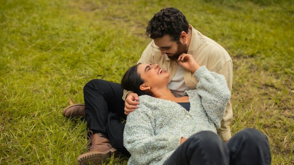 A happy couple sitting on a grassy field.