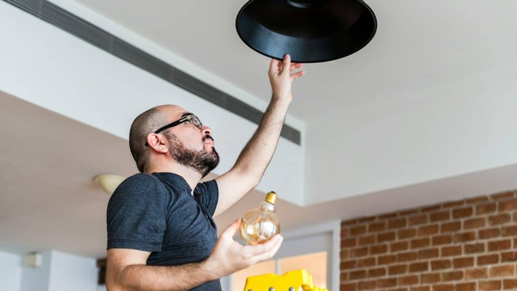 A bald man wearing glasses is changing a lightbulb. 