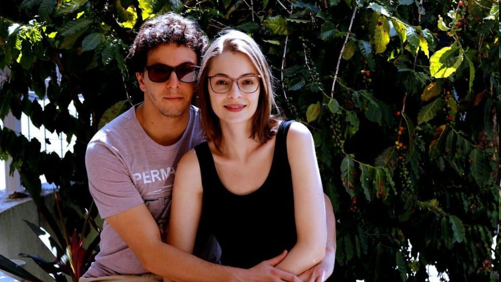 A man wearing sunglasses is holding a bespectacled woman.