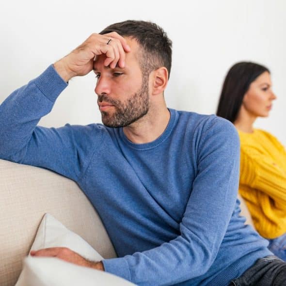 A man looking frustrated while a woman sits in the background.