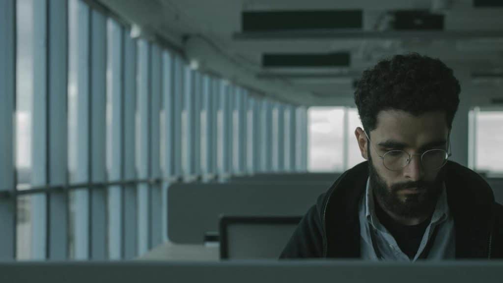 A man wearing glasses sitting alone in an empty office, focused on his work.