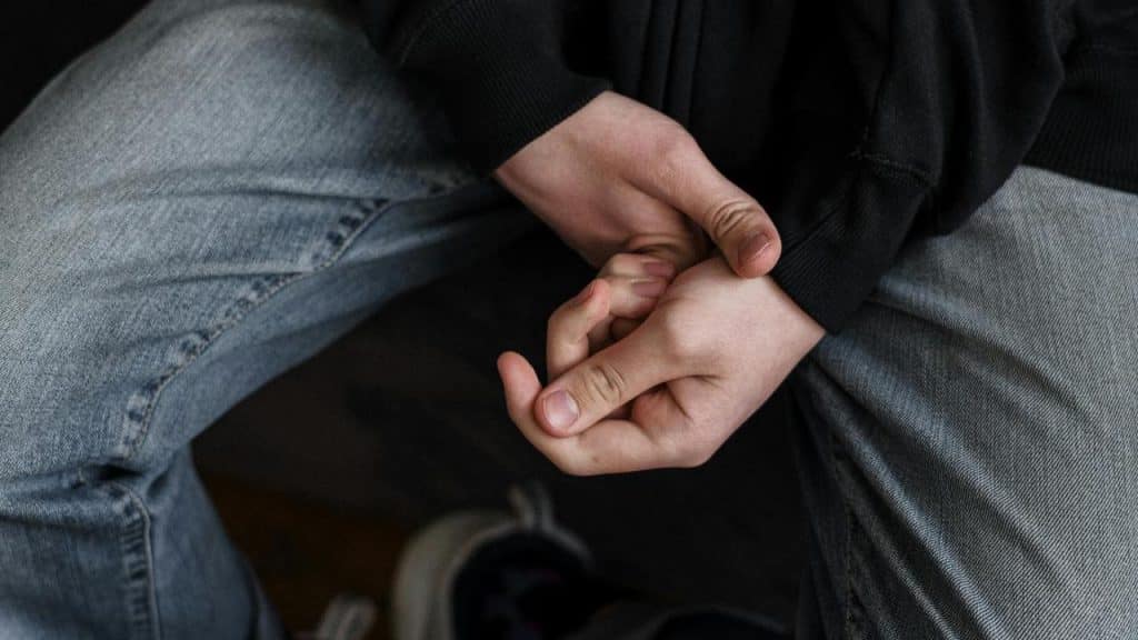 A person sitting with hands clasped together in their lap.