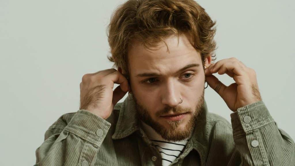 A man adjusting his earphones while looking focused and pensive.