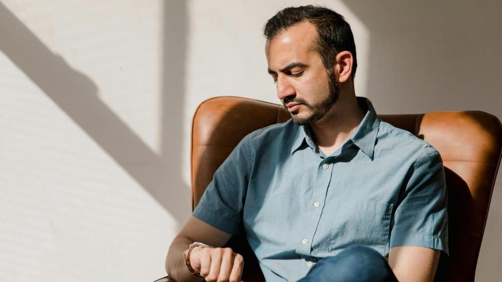 A man sitting in a leather chair, looking down thoughtfully in warm sunlight.